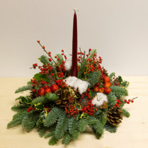 Centrotavola Buone Feste natalizio con candela rossa, rami di abete, pigne, bacche e cotone