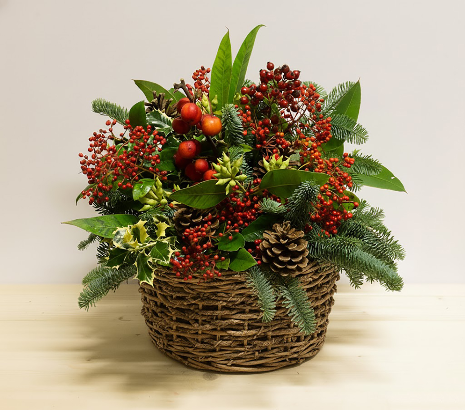 Incanto Natalizio; composizione con rose rosse, agrifoglio, bacche e pino in cestino tondo bianco.