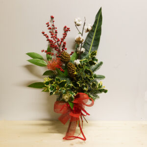 Spirito di Natale: mazzo natalizio con bacche rosse, cotone, agrifoglio, pigne e fiocco in rete rossa.