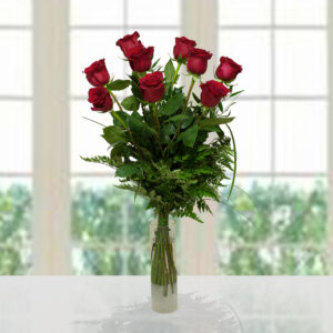 Ricco bouquet di 9 rose rosse di alta qualità con foglie verdi e felci decorative in vaso cilindrico trasparente, sfondo luminoso.