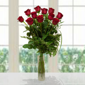 Grande bouquet di 11 rose rosse premium con verde decorativo e felci in un vaso di vetro cilindrico, illuminazione naturale.