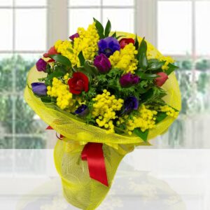 Ricco bouquet di anemoni colorati (blu, viola, rossi) e mimosa gialla, confezionato con rete gialla e fiocco rosso.