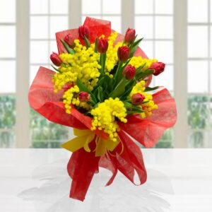 Mazzo di tulipani rossi e mimosa gialla, confezionato con carta velina rossa e fiocco giallo su sfondo luminoso.